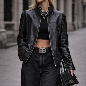 Könnte beinhalten: Eine weiße Keramik-Tasse mit schwarzem Henkel und dem Text "But First, Coffee" in schwarzer, handschriftlicher Schrift. Die Tasse steht auf einer weißen Oberfläche.