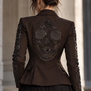 Könnte beinhalten: Ein dunkelbrauner Blazer mit einem aufwendigen, schwarzen Perlen-Totenkopf-Design auf dem Rückenteil. Die Ärmel sind mit schwarzen Perlen und Pailletten in geometrischen Mustern verziert. Die Jacke hat eine taillierte Passform mit Schößchen.