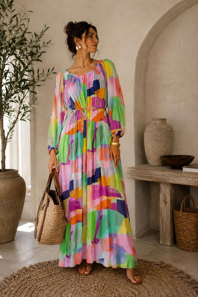 Pu&ograve; includere: Un lungo abito colorato con un motivo geometrico nei toni del rosa, verde, blu e arancione. L'abito ha maniche lunghe e vita stretta. Una borsa tote in paglia con manici in pelle &egrave; tenuta in mano.