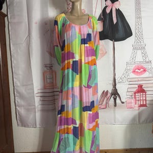 Pu&ograve; includere: Un lungo abito colorato con un motivo geometrico nei toni del rosa, verde, viola e blu &egrave; esposto su un manichino. L'abito ha uno scollo tondo e maniche lunghe. Lo sfondo include un fondale decorativo con illustrazioni a tema moda.