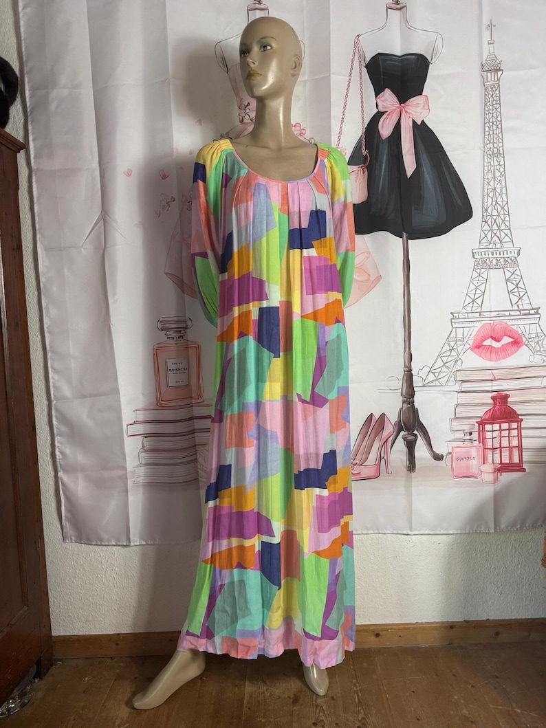 Pu&ograve; includere: Un lungo abito colorato con un motivo geometrico nei toni del rosa, verde, viola e blu &egrave; esposto su un manichino. L'abito ha uno scollo tondo e maniche lunghe. Lo sfondo include un fondale decorativo con illustrazioni a tema moda.