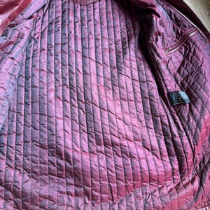 K&ouml;nnte beinhalten: Eine bordeauxrote Lederjacke mit gestepptem Innenfutter. Das Innenetikett tr&auml;gt den Text MORENA ART OF FASHION. Die Jacke verf&uuml;gt &uuml;ber ein vertikales Steppmuster auf der Innenseite, eine kleine Innentasche und ein schwarzes Pflegeetikett.