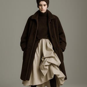 Könnte beinhalten: Eine Frau trägt einen braunen Mantel, einen Rollkragenpullover und einen turbanartigen Hut. Das Outfit umfasst einen beigen Rock mit drapiertem Design, schwarze Strumpfhosen und schwarze Stiefeletten. Das Ensemble ist ein modisches Statement.