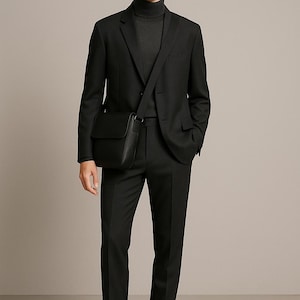 Könnte beinhalten: Eine Person in einem schwarzen Anzug, einem schwarzen Rollkragenpullover und einer Sonnenbrille. Der Anzug besteht aus einem Blazer und einer maßgeschneiderten Hose. Eine schwarze Leder-Umhängetasche wird quer über dem Körper getragen. Schwarze Sneaker vervollständigen das Outfit.