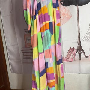 Pu&ograve; includere: Un abito lungo e fluido con un colorato motivo geometrico. L'abito presenta una variet&agrave; di colori, tra cui rosa, giallo, verde, arancione e viola. L'abito ha una vestibilit&agrave; ampia e comoda e uno scollo tondo.