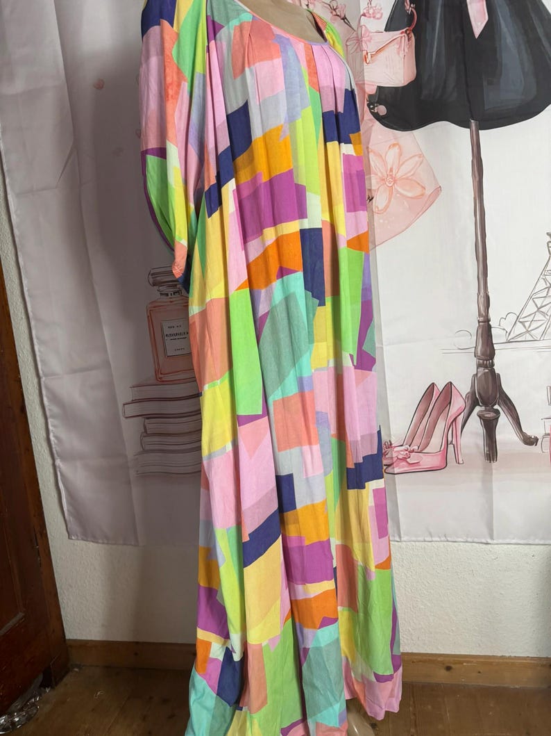 Pu&ograve; includere: Un abito lungo e fluido con un colorato motivo geometrico. L'abito presenta una variet&agrave; di colori, tra cui rosa, giallo, verde, arancione e viola. L'abito ha una vestibilit&agrave; ampia e comoda e uno scollo tondo.