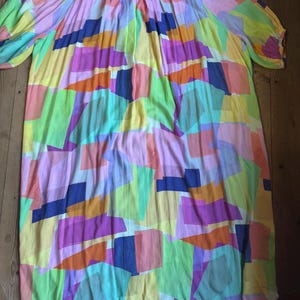 Pu&ograve; includere: Un abito colorato e ampio con un motivo geometrico. L'abito presenta uno scollo tondo e maniche corte a sbuffo. Il design incorpora vari colori, tra cui rosa, giallo, verde, arancione e blu, creando un look vibrante e accattivante.