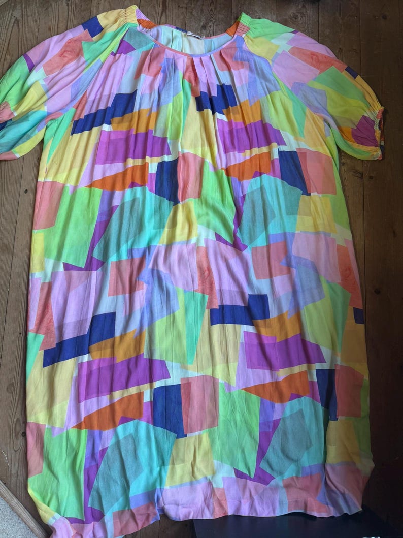 Pu&ograve; includere: Un abito colorato e ampio con un motivo geometrico. L'abito presenta uno scollo tondo e maniche corte a sbuffo. Il design incorpora vari colori, tra cui rosa, giallo, verde, arancione e blu, creando un look vibrante e accattivante.