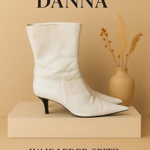Könnte beinhalten: Weiße Leder-Ankle Boots mit spitzer Zehenpartie und kleinem schwarzem Absatz. Die Stiefel werden auf einer beigefarbenen Plattform präsentiert, mit dem Text "VERONIKA DANNA" und "WAIF LEDER SPITZ ANKLE BOOTS" in Schwarz.