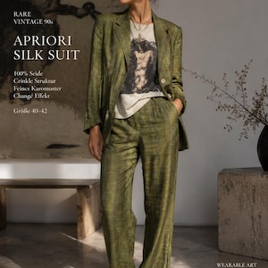 Op de afbeelding: Een groene zijden broekpak met een ruitpatroon. Het pak bestaat uit een blazer en een broek met wijde pijpen. De tekst op de afbeelding luidt "APRIORI SILK SUIT" en "RARE VINTAGE 90s". Het model draagt een grafisch T-shirt en een zonnebril.