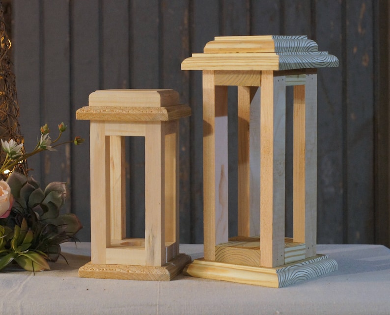 May include: Two wooden candle lanterns, one larger than the other, with a natural wood finish. The larger lantern has a blue and white striped base.