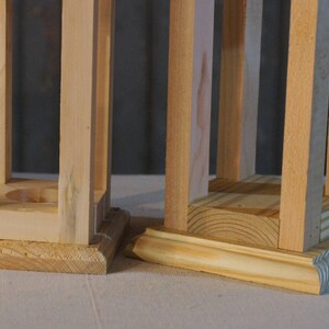 May include: Two unfinished wooden lanterns with square bases. The lantern on the left has a simple base, while the lantern on the right has a more decorative base.