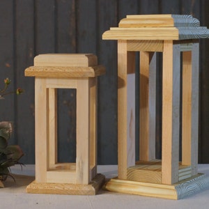 May include: Two wooden candle lanterns, one larger than the other, both with a simple rectangular design. The larger lantern has a light blue painted base.
