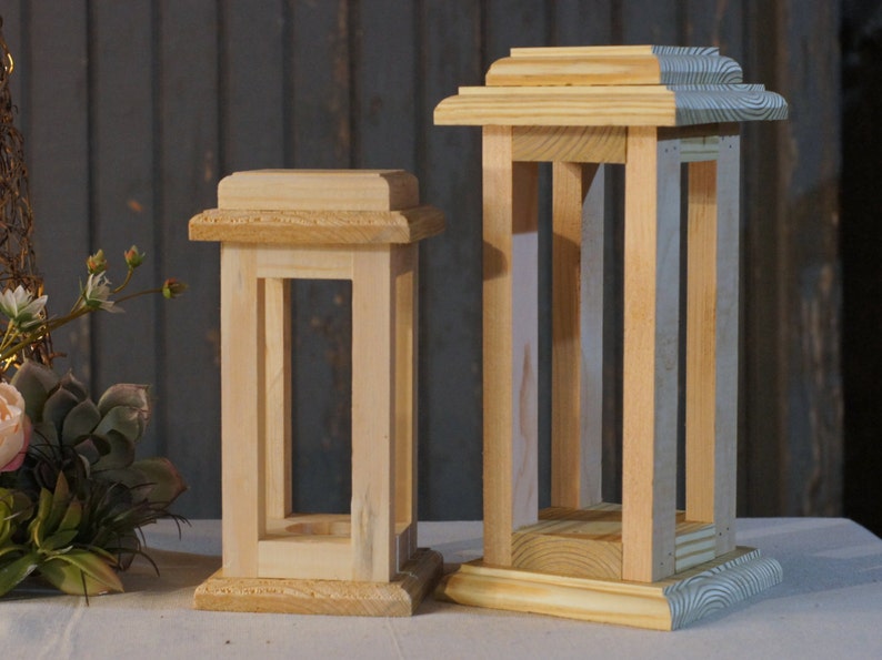 May include: Two wooden candle lanterns, one larger than the other, both with a simple rectangular design. The larger lantern has a light blue painted base.