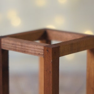 May include: A wooden square frame made of light brown wood. The frame is empty and has a smooth finish.