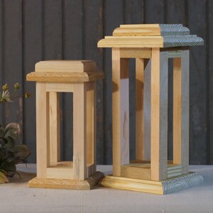 May include: Two wooden candle lanterns, one is natural wood and the other is painted with a blue and white pattern. The lanterns are both rectangular and have a square base.