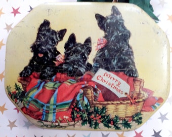 May include: Vintage Christmas tin with a yellow background featuring three black Scottish Terriers nestled in a red and green plaid blanket. The dogs are sitting in a wicker basket with a "Merry Christmas" tag. The tin has a slightly oval shape.