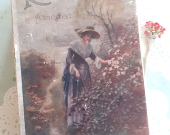 May include: Vintage Rowntree's Assorted Chocolates box with a faded image of a woman in a long dress and hat standing in a garden with pink flowers. The text "Rowntree's Assorted Chocolates" is printed on the box.