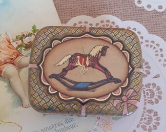 May include: A vintage-style tin box with a rocking horse design. The box has a brown, pink, and green checkered pattern with a gold trim. The rocking horse is painted in shades of pink, red, and white.
