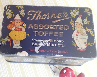 May include: Vintage blue metal Thorne's Assorted Toffee tin. The tin features illustrations of children in whimsical outfits, floral accents, and the text "Thorne's Assorted Toffee". The tin is rectangular and shows signs of wear.