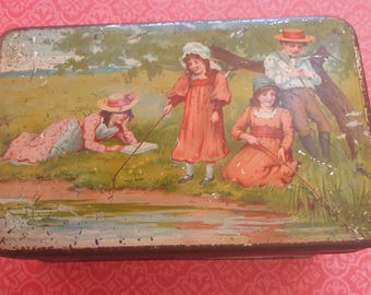 May include: Vintage tin box with a colorful illustration of four children fishing by a river. The children are wearing hats and dresses, and the scene is set in a lush green meadow.