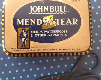 May include: A vintage tin of John Bull Mend-A-Tear fabric repair product. The tin is brown with gold lettering and a blue oval containing an illustration of a man holding a stick and a small iron. The text on the tin reads "John Bull Mend-A-Tear Mends Waterproofs & Other Garments Trade Mark Made in England by John Bull Rubber Co. Ltd., Leicester."