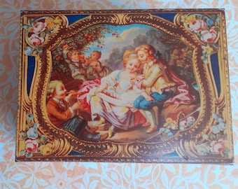 May include: Rectangular box with a detailed, framed painting of a romantic scene. The painting features figures in period clothing, surrounded by floral and ornate gold detailing. The box has a blue border and is set against a patterned background.