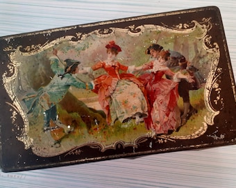 May include: Rectangular vintage tin with a painted scene of people dancing in period clothing. The tin has a black background with gold decorative trim and a slightly distressed appearance.