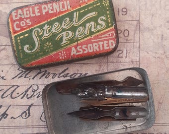 May include: Vintage metal pen tins. One tin is rectangular with the text "EAGLE PENCIL Co's Steel Pens ASSORTED" in red and green. The other tin contains several steel pen nibs. The background is a vintage paper.