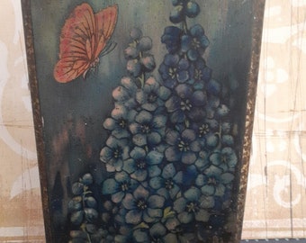 May include: A wooden plaque with a painted image of blue flowers and an orange butterfly. The background is a dark blue and green.