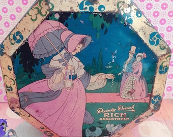 May include: A vintage tin box with a colorful illustration of a woman in a pink dress and a blue umbrella. The text on the box reads "Dainty Dinah Rich Assortment".