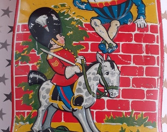 May include: A vintage tin lunchbox featuring Humpty Dumpty sitting on a brick wall with a toy soldier riding a rocking horse. The lunchbox is yellow with red and green accents.