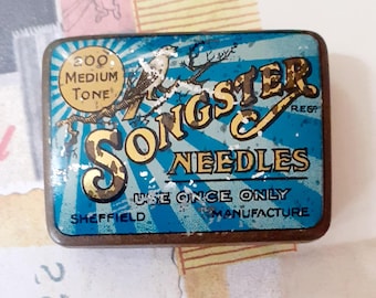 May include: A rectangular, vintage Songster Needles tin. The tin features a blue and white striped background with gold lettering and a bird illustration. Text includes "Songster Needles", "Use Once Only", and "Sheffield Manufacture".
