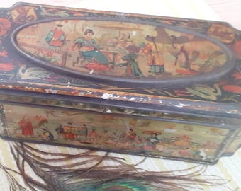 May include: An antique, oval-shaped tin box with a black exterior and a decorative lid featuring a painted scene of people in traditional clothing. The box has a distressed appearance, with visible wear and tear, and red dragon accents.