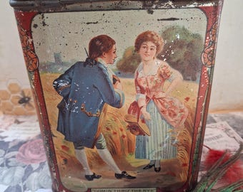 May include: A rectangular metal tin with a hinged lid, featuring a vintage illustration of two figures in a field with the text "COMIN' THRO THE RYE" at the bottom. The tin has a distressed red border and shows signs of wear on the surface.