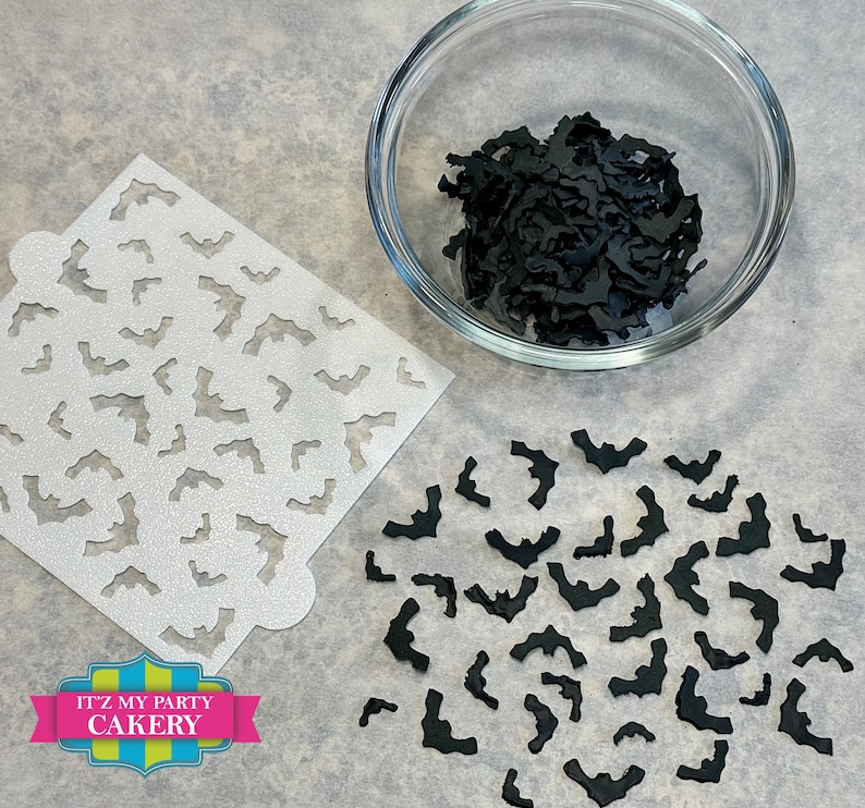 May include: A white stencil with a repeating pattern of bats, a bowl filled with black bat cutouts, and a scattering of black bat cutouts on a white surface. The text "It'z My Party Cakery" is printed on a blue, green, and yellow banner.