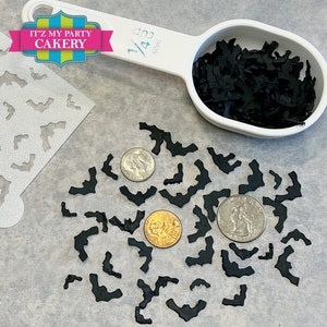 May include: Black bat sprinkles for decorating cakes and cupcakes. The sprinkles are shown in a measuring cup and scattered on a table with a stencil and coins for size reference.