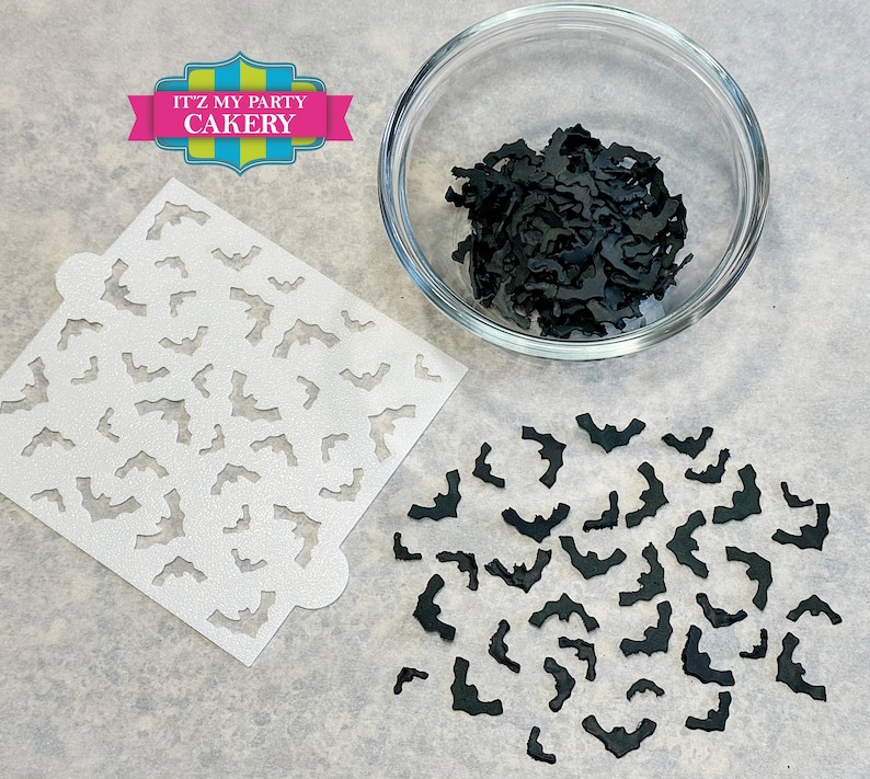 May include: A white stencil with a repeating pattern of bats, a bowl of black bat sprinkles, and a scattering of black bat sprinkles on a gray surface. The stencil is labeled "It'z My Party Cakery".