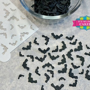 May include: A white stencil with a repeating pattern of bats, next to a bowl of black fondant bats. The bowl is on a white surface. The text "IT'Z MY PARTY CAKERY" is in the upper right corner of the image.