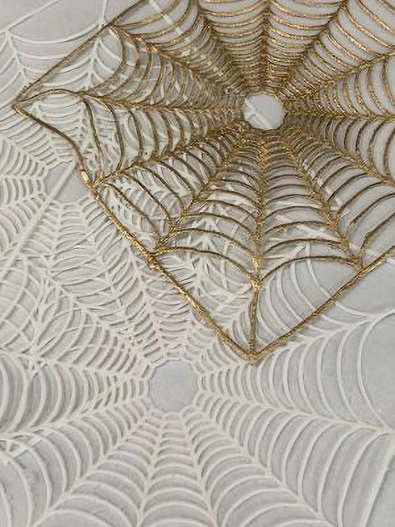 May include: A white and gold spiderweb design with a raised texture. The design is made of two layers, one on top of the other. The top layer is gold and the bottom layer is white.