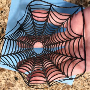 May include: Black spiderweb cutout, a decorative element for Halloween crafts and decorations.