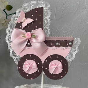 Peut inclure: Un topper de g&acirc;teau de chariot de b&eacute;b&eacute; rose et marron avec un n&oelig;ud rose, un papillon rose et une bordure en dentelle blanche. Le chariot est d&eacute;cor&eacute; de pois blancs.