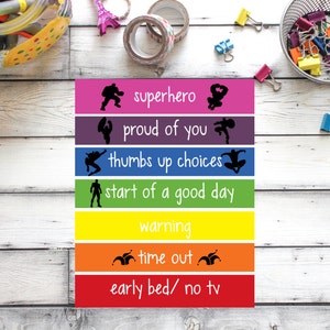 Puede incluir: Un conjunto de tiras de colores arcoíris con frases de refuerzo positivo y negativo para niños. Las frases incluyen "superhéroe", "orgulloso de ti", "elecciones con pulgares arriba", "comienzo de un buen día", "advertencia", "tiempo fuera" y "cama temprano/ sin televisión".