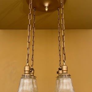 May include: A vintage-style chandelier with a gold-toned canopy and chains. The chains support three clear, ribbed glass shades. The fixture is designed for overhead lighting and adds a classic touch to any room.