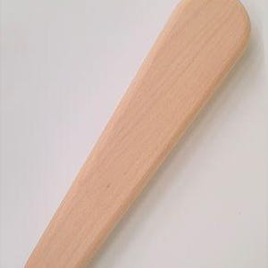 May include: A light-colored, wooden shoe horn with a rounded top and a tapered, elongated body. The wood grain is visible, and the horn is smooth and unadorned.