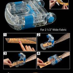 May include: A clear and blue Magic Binding Maker with Binding Spool, designed for 2 1/2" wide fabric. The image shows the tool and steps for creating sharp crease binding. The text reads "Magic Binding Maker" and "No-Iron E-Z Fold Binding."