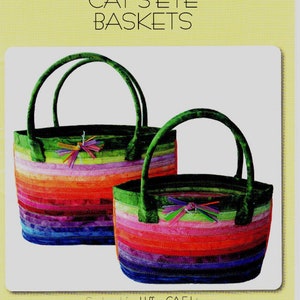 May include: Two Cat's Eye Baskets pattern. The baskets are colorful, with horizontal stripes in shades of red, orange, purple, and green. They have green handles and decorative accents. The text "AUNTIES TWO PATTERNS" and "CAT'S EYE BASKETS" is visible.