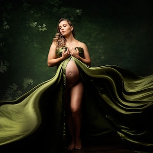 May include: A pregnant person draped in flowing olive green fabric. The fabric is wrapped around the chest and cascades down, creating a dramatic effect. The background is a dark green with subtle leaf patterns.