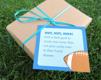May include: A brown gift box tied with a turquoise ribbon and a blue card with the text "HUT, HUT, HIKE! Kick a field goal to score one more, then run your socks over to their home drawer." and a cartoon football.