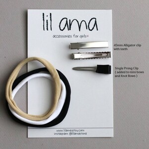 May include: A set of hair accessories for girls, including three elastic headbands in black, white, and beige, a 45mm alligator clip with teeth, and a single prong clip. The text "lil ama accessories for girls" is printed on the white card.
